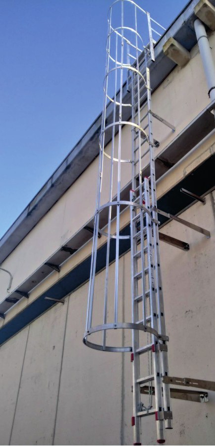Escada marinheiro de alumínio com gaiola de proteção instalada na fachada de um prédio industrial